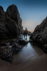 Man standing on rock by sea against sky