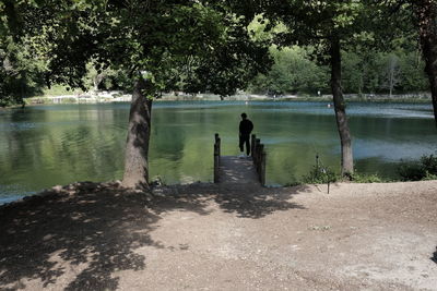 Rear view of silhouette man standing on pier by trees at lago sinizzo lake