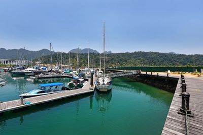 Boats moored at harbor against clear blue sky