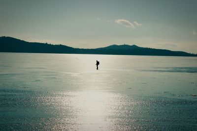 Silhouette man ice-skating on frozen lake against sky