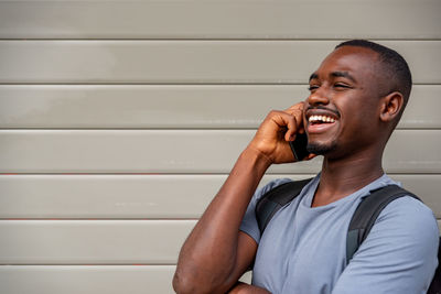 Smiling young man talking on phone against wall