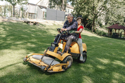 Senior couple sitting on lawn mower in backyard