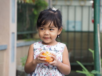 A beautiful asian kid girl wearing butterflies dress smiling while holding an orange fruit