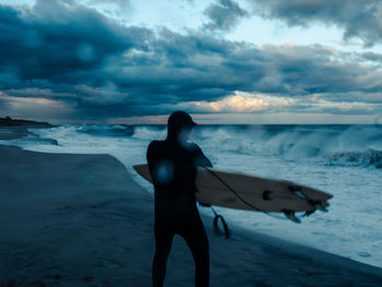 Rear view of man with surfboard standing on shore at beach