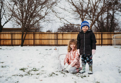 Young brother and sister building a snowman outside in winter