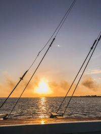 Silhouette fishing rod by sea against sky during sunset