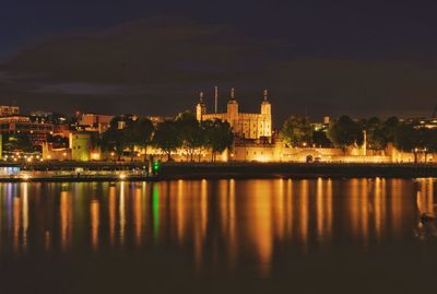 Illuminated buildings by lake against sky at night