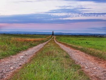Road amidst field against sky during sunset
