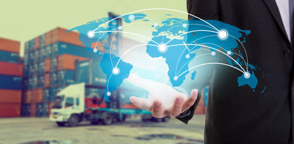 Midsection of businessman holding digital world map against cargo container