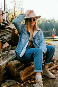 Portrait of young woman wearing hat sitting by wooden pile