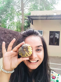 Portrait of smiling young woman holding fruit against eye