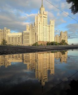 Modern buildings with reflection on puddle against cloudy sky