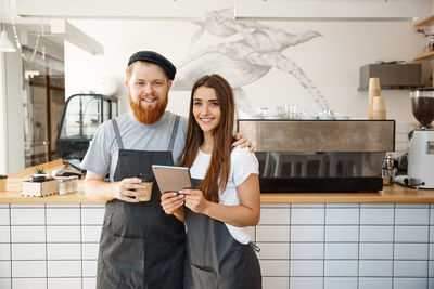 Portrait of smiling young woman using mobile phone while standing in cafe