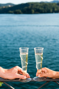 Close-up of couple hands holding champagne on railing by sea