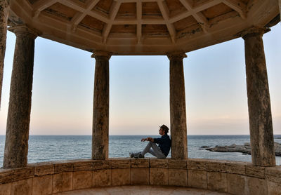 Side view of man sitting in gazebo against sea