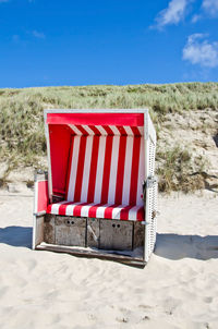 Red hooded chairs on beach against sky on sunny day