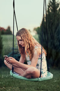 Girl using mobile phone while sitting on swing