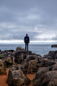 Rear view of woman walking on rock by sea against sky