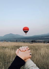 Cropped image of couple holding hands against hot air balloon over landscape