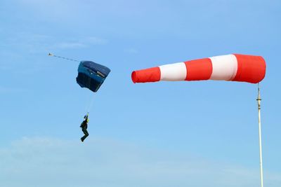 Low angle view of man paragliding by windsock against blue sky