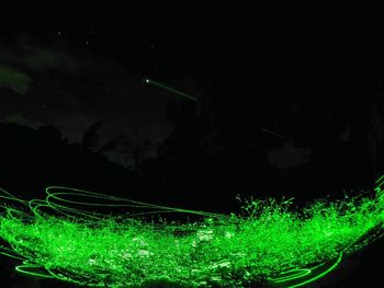 Illuminated light trails on landscape against sky at night