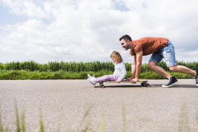 Father pushing daughter on skateboard