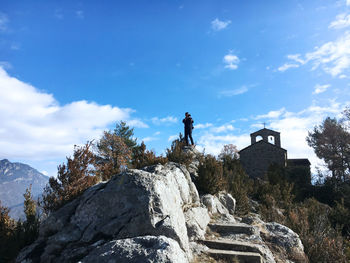 Man photographing while standing on rock against blue sky