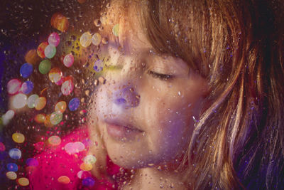 Close-up of cute girl by wet glass window