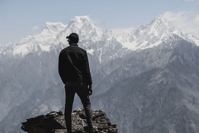 Rear view of man standing on rock against snowcapped mountains