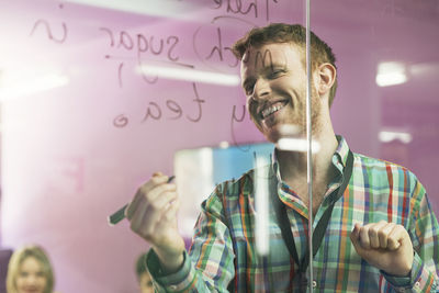 Smiling businessman writing on glass wall during meeting