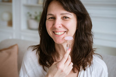 Portrait of caucasian woman doing facial massage with quartz scraper for pink