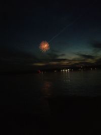 Firework display over sea against sky at night