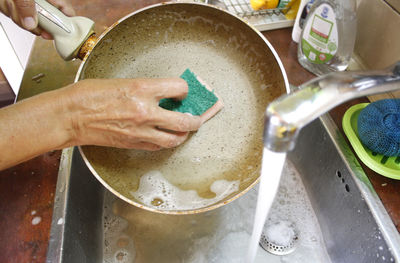 Cropped hand washing cooking pan in sink