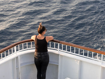 Rear view of man standing on railing against sea