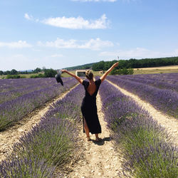 Rear view of woman with arms raised on field against sky