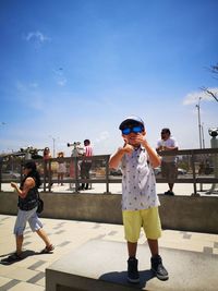 Full length of friends on skateboard against blue sky