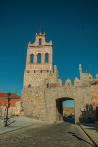 Street going through the carmen gateway on the stone city wall and brick tower in avila, spain.