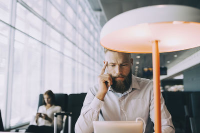 Businessman watching video on digital tablet while sitting at table in airport departure area