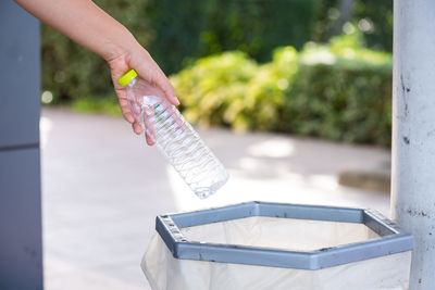 Close-up of hand throwing bottle in garbage bin