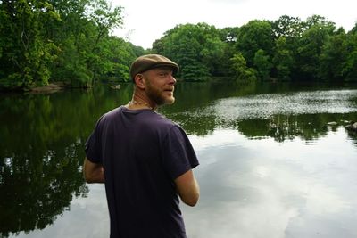 Young man standing by lake against trees