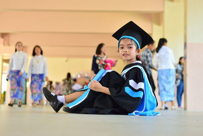 Portrait of girl wearing graduation gown and mortarboard while sitting on floor