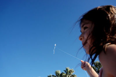 Low angle view of girl holding kite against blue sky