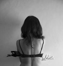 Rear view of woman wearing bra standing against wall