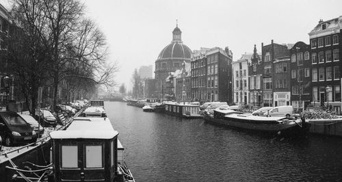 Boats in canal amidst buildings in city against sky on a winter day