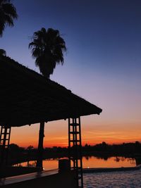 Silhouette palm trees by sea against sky during sunset