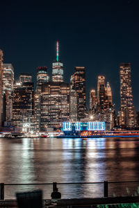 Illuminated buildings by river against sky at night