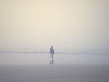 Rear view of woman standing at sea shore during foggy weather