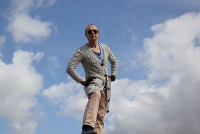 Low angle portrait of mature man with hands on hip standing against cloudy sky
