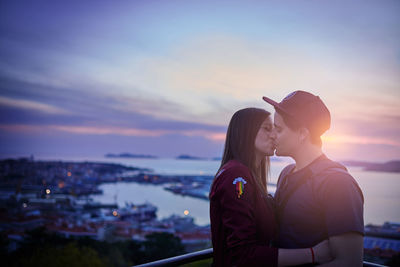 Couple kissing while standing against sea during sunset