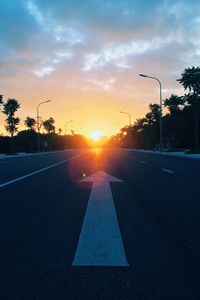 Road by silhouette trees against sky during sunset